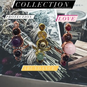 May include: Three wire-wrapped rings with different colored stones. The rings are labeled "Protection", "Love", and "Abundance".