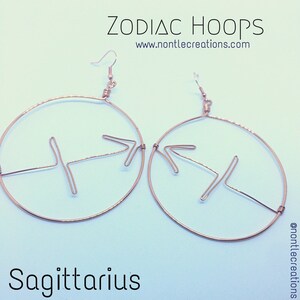 Puede incluir: Aretes de aro dorados con un s&iacute;mbolo del zod&iacute;aco Sagitario. Los aretes est&aacute;n hechos de alambre y tienen un dise&ntilde;o simple. El texto "ZODIAC HOOPS" y "www.nontlecreations.com" es visible en la imagen.