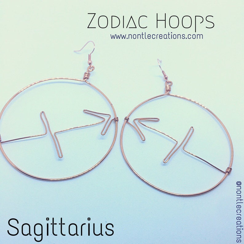 Puede incluir: Aretes de aro dorados con un s&iacute;mbolo del zod&iacute;aco Sagitario. Los aretes est&aacute;n hechos de alambre y tienen un dise&ntilde;o simple. El texto "ZODIAC HOOPS" y "www.nontlecreations.com" es visible en la imagen.