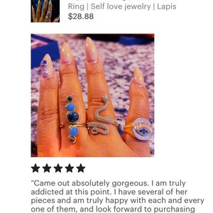 May include: A hand wearing several rings, including a snake ring, a ring with a blue eye, and a ring with blue and green stones. The rings are on a finger with nude nail polish. "Came out absolutely gorgeous. I am truly addicted at this point. I have several of her pieces and am truly happy with each and every one of them, and look forward to purchasing more!"