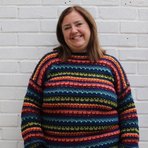 May include: A woman wearing a colourful striped crochet sweater with blue jeans.