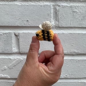 Puede incluir: Una pequeña abeja de crochet con rayas amarillas y negras y alas blancas. La abeja está siendo sostenida por una mano.