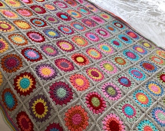May include: A colorful crocheted throw blanket with a gray background and a variety of bright colors, including pink, red, yellow, blue, and green. The blanket is made up of a series of squares, each with a different pattern.