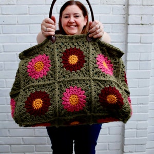 May include: A large green crocheted tote bag with pink and burgundy flowers. The bag has brown leather handles.