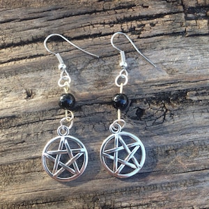 May include: A pair of silver earrings with a black bead and a silver pentacle charm.