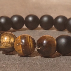 May include: A bracelet made of black and brown beads. The bracelet has two larger brown beads with a tiger's eye pattern.