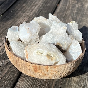 May include: A bowl of white agate crystal chunks. The bowl is made of natural coconut shell. The crystals are translucent and have a milky white color.