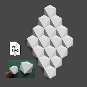 Może przedstawiać: Biała papierowa rzeźba ścienna w stylu geometrycznym wykonana z trójwymiarowych trójkątów. Rzeźba ma kształt rombu i składa się z 20 pojedynczych trójkątów. Rzeźba jest pokazana na ciemnoszarym tle. Pliki PDF i SVG są dostępne do pobrania.