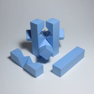 May include: A blue geometric puzzle made of paper. The puzzle is assembled into a star shape with four arms and a central piece. The puzzle is made of five pieces.