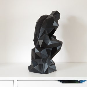 May include: A black, geometric sculpture of a person sitting with their head in their hand. The sculpture is made of many small triangles and has a modern, abstract style.