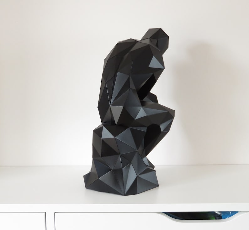 May include: A black, geometric sculpture of a person sitting with their head in their hand. The sculpture is made of many small triangles and has a modern, abstract style.