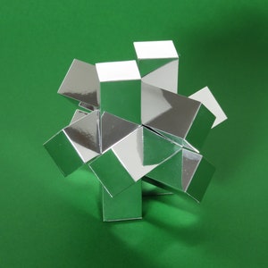 May include: A silver geometric puzzle made of multiple interlocking cubes. The puzzle is assembled into a star shape and is sitting on a green surface.