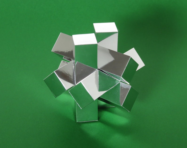 May include: A silver geometric puzzle made of multiple interlocking cubes. The puzzle is assembled into a star shape and is sitting on a green surface.