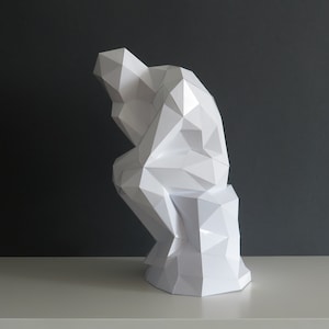 May include: A white paper sculpture of a person sitting in a thinking pose. The sculpture is made of many small triangles and is very detailed.
