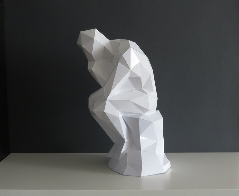 May include: A white paper sculpture of a person sitting in a thinking pose. The sculpture is made of many small triangles and is very detailed.