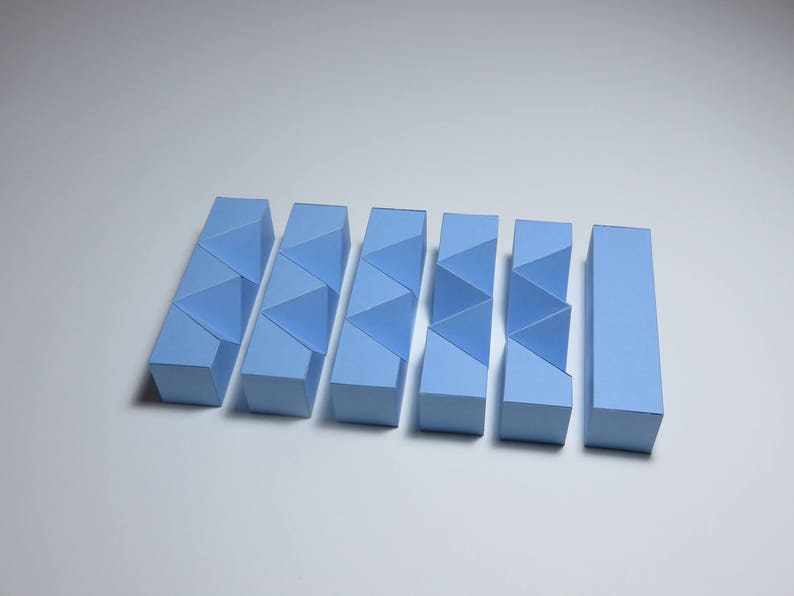 May include: A set of seven light blue geometric puzzle pieces made of paper. The pieces are arranged in a row and are all the same size and shape.