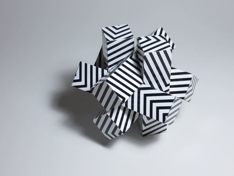 May include: A group of black and white striped geometric shapes are arranged in a cluster. The shapes are made of paper and have a three-dimensional appearance.