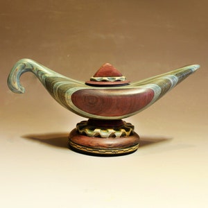 Puede incluir: Una lámpara de genio de madera con un cuerpo rayado verde y marrón, una tapa roja y una base detallada con un diseño de engranaje.