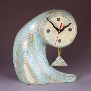 May include: A blue and white wooden clock with a pendulum. The clock is shaped like a wave and has a unique design.
