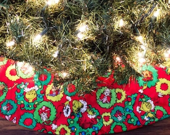 May include: A red Christmas tree skirt with a green and yellow print of characters from the Grinch movie. The skirt is decorated with wreaths and the characters are wearing Santa hats.