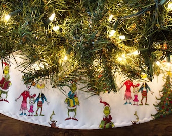 May include: A white Christmas tree skirt with a green, red, and yellow Grinch and Whoville character print. The skirt is decorated with a white scalloped edge and a white satin ribbon.