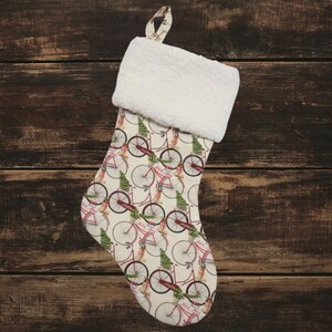 May include: A white Christmas stocking with a cream-colored cuff. The stocking is decorated with a repeating pattern of red bicycles with green trees.