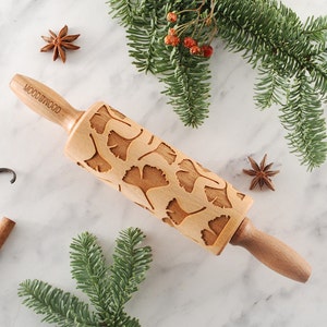May include: A wooden rolling pin with a ginkgo leaf design. The rolling pin is on a white marble surface with cinnamon sticks, vanilla beans, and star anise.