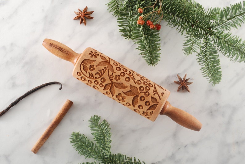 Puede incluir: Un rodillo de madera con un dise&ntilde;o floral grabado en la superficie. El rodillo est&aacute; hecho de madera natural y tiene un mango con la palabra "MOODWOOD" grabada en &eacute;l.