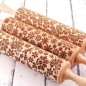 three wooden rolling pins laser engraved with 3 different floral patterns. They are on white board rustic background.