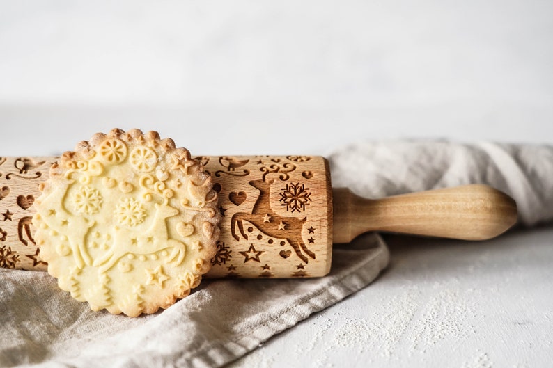 wooden rolling pin withdesign of reindeer. A big well baked round biscuit is standing in front of it.