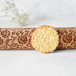 Wooden rolling pin with decorative design of polish folk traditional flowers. A well baked cookie presenting the effects of embossing is standing in front of it.