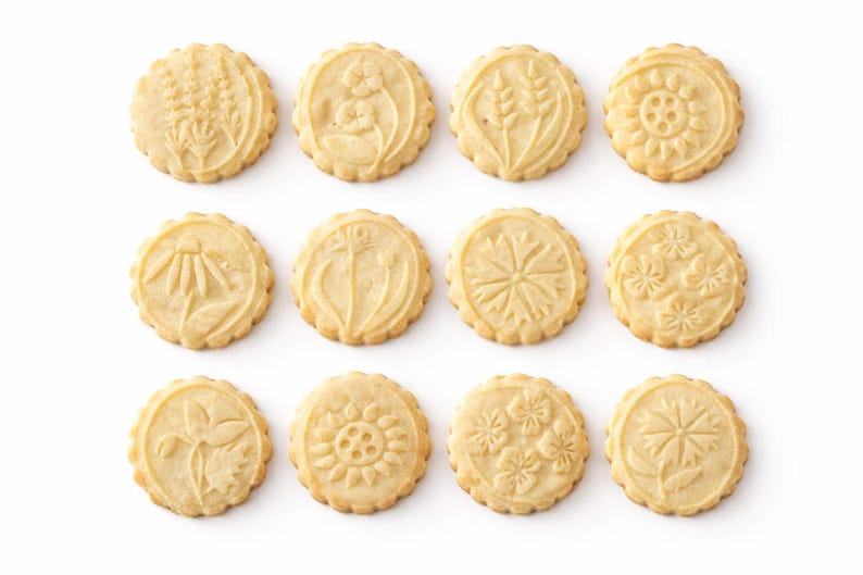 Minimalist product composition featuring nine embossed botanical cookies arranged in a neat grid on a bright white background. On the right, elegant serif headline reads “Real baking results,” followed by a refined benefits list with icons, highlighting texture, timeless design, uniqueness, gifting appeal, customization, and creative baking. Soft shadows, warm tones, and luxury-style typography create a premium, high-end visual feel.