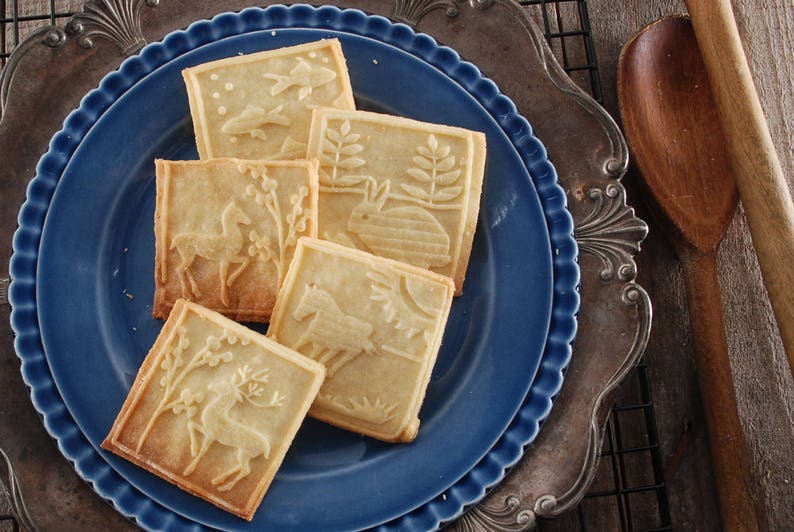 Cookies made with the rolling pin. rectangular,each has a different animal on it. Cookies are lying on the dark blue plate, standing on a silverplated metal dish with decorative art nuveau rim.