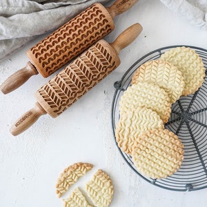 Set of two mini rolling pins with knitt stiches design. Several cookies with embossed design are on a metal trivet.
