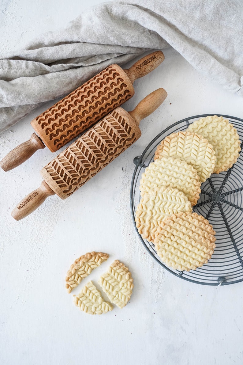 Set of two mini rolling pins with knitt stiches design. Several cookies with embossed design are on a metal trivet.