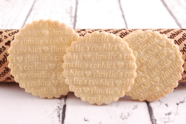 May include: Three round, light brown cookies with the text "Amelie's cookies" repeated on each cookie. The cookies are decorated with small heart shapes.