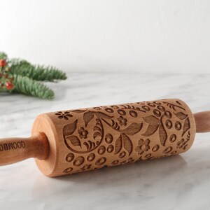 Puede incluir: Un rodillo de madera con un dise&ntilde;o floral grabado en la superficie. El rodillo tiene un mango de madera marr&oacute;n con la palabra "MOODWOOD" grabada en &eacute;l.