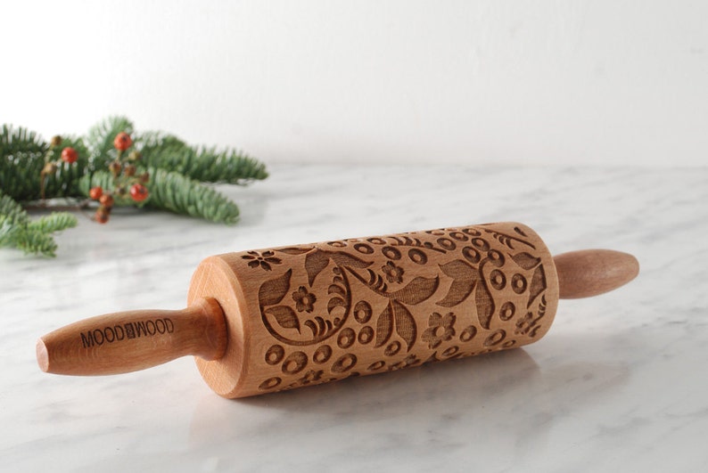 Puede incluir: Un rodillo de madera con un dise&ntilde;o floral grabado en la superficie. El rodillo tiene un mango de madera marr&oacute;n con la palabra "MOODWOOD" grabada en &eacute;l.