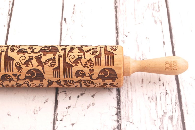 Wooden rolling pin laser engraved with design of tropical animals such as elephants, giraffs, parrots, monkeys, surrounded by palm and monstera leaves.