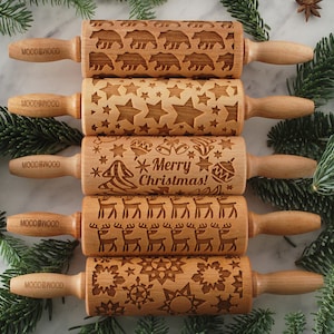 Five small wooden rolling pins with laser engraed designs on them: snowflakes, reindeer, merry christmas text, stars and polar bears. Among christmas tree branches.