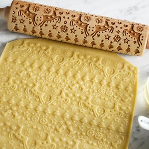 A  big slab of dough with embossed reindeer decorative pattern, with wooden rolling pin for embossing.