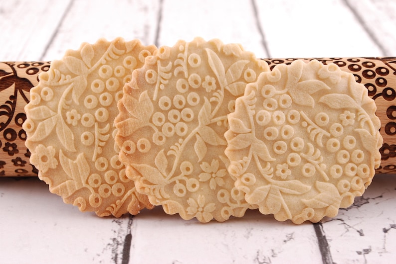 Puede incluir: Tres galletas redondas de color marr&oacute;n claro con un dise&ntilde;o floral en relieve en la superficie. Las galletas est&aacute;n sobre una superficie de madera blanca.