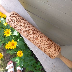 Wooden embossing rolling pin with moodforwood logo on the handle, embossing design is rosemaling, norwegian folk. yellow flowers on the left.