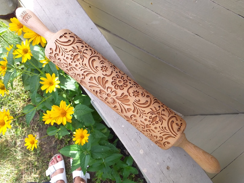 Wooden embossing rolling pin with moodforwood logo on the handle, embossing design is rosemaling, norwegian folk. yellow flowers on the left.