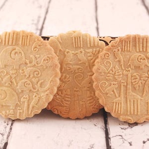 Three big round cookies are standing in front of wooden rolling pin.