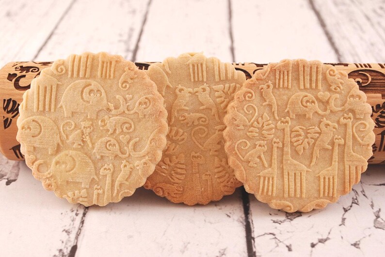 Three big round cookies are standing in front of wooden rolling pin.