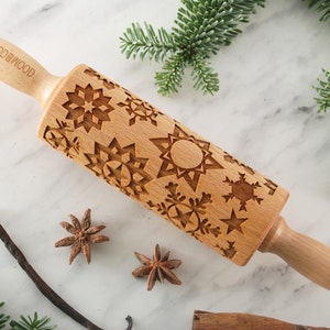 Small wooden rolling pin with snowflake design for embossing cookies. I is lying among christmas tree green branches, vanilla pod and anise seeds