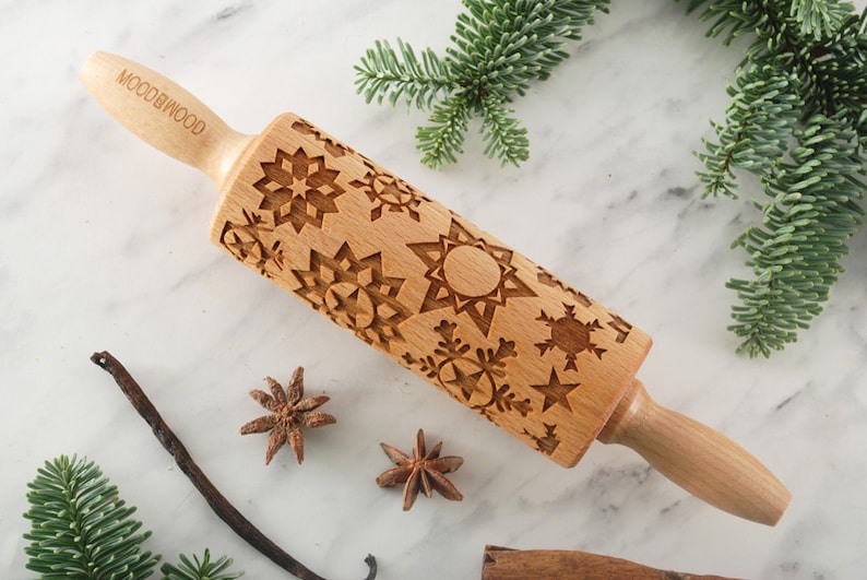 Small wooden rolling pin with snowflake design for embossing cookies. I is lying among christmas tree green branches, vanilla pod and anise seeds