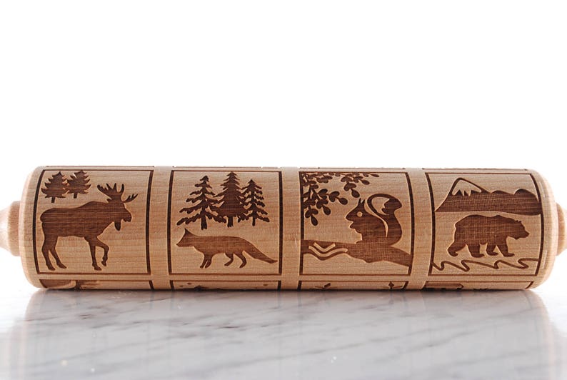 Wooden rolling pin laser engraed to make biscuits with different animal designs. Cow and rabbit are at the front.