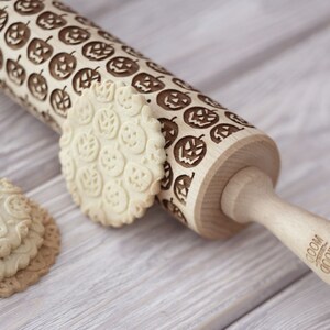 A pile of well baked cookies with embossed design is in front of a rolling pin